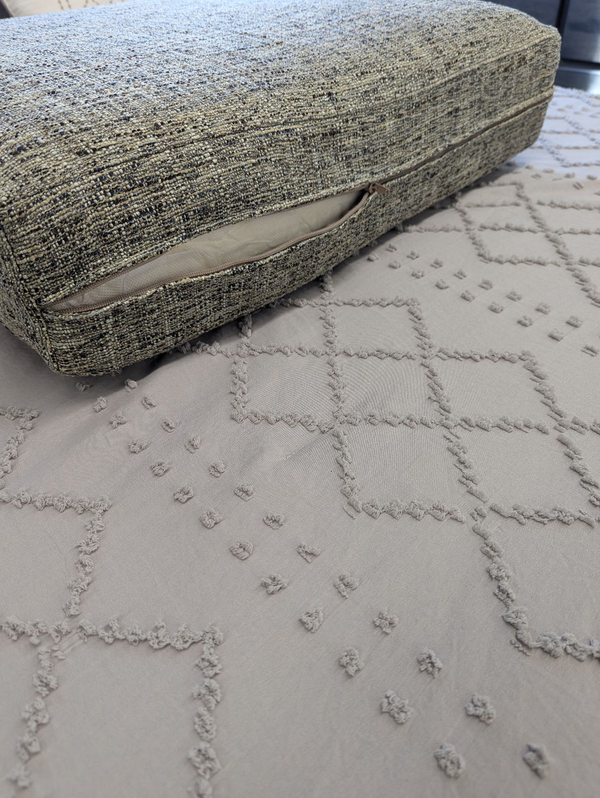 Close-up of a tweed replacement cushion showing the zippered side closure and inner liner on a beige quilted bedspread