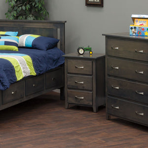 Gray stained 3-drawer nightstand between a storage bed and matching chest of drawers in a boy's bedroom with navy bedding