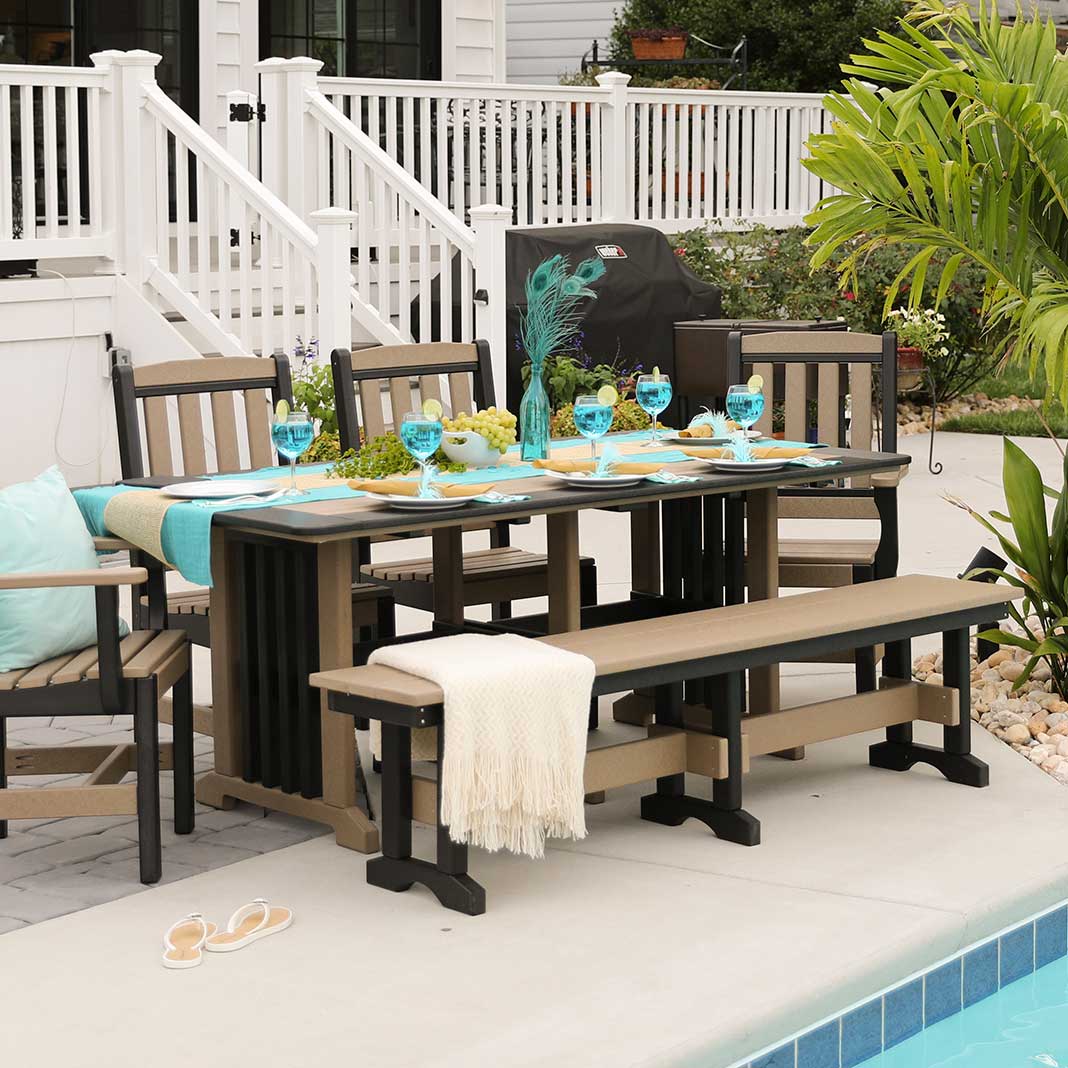 Weatherwood and black poly dining table with chairs and a bench set with teal linens beside a backyard pool