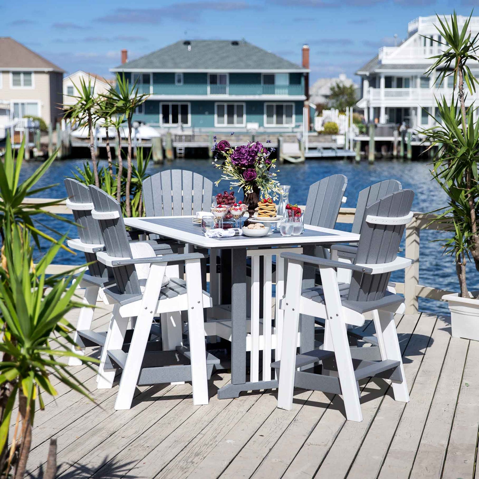 Gray and white poly counter height patio table with six tall Adirondack chairs set on a bayfront dock