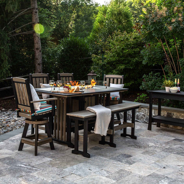 Rustic gray and black poly fire pit bar table with swivel chairs, a bench and wine glasses on a patio
