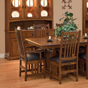 Mission oak dining chairs with vertical slat backs and black leather seats at a trestle table by a hutch