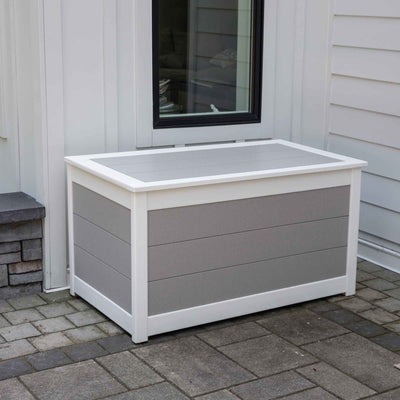 White and gray poly deck box with plank lid and horizontal panels beside a window on a paver patio