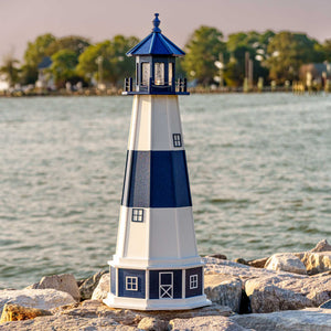 Navy and white banded lighthouse with blue lantern room on a white base with navy panels, set on a rocky shoreline