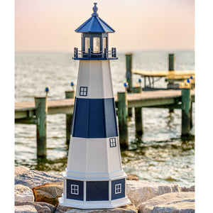Navy and white lighthouse with blue lantern room standing on rocks by a dock and calm bay water