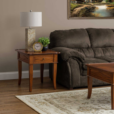 Cherry end table with a single ring pull drawer and curved legs beside a sofa with a lamp and small clock