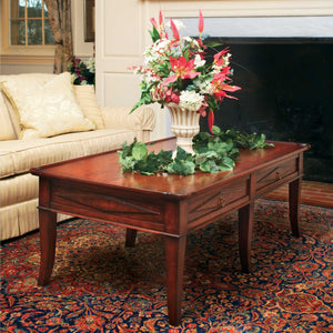 Cherry Victorian coffee table with two drawers and flared legs styled with a floral urn in front of a fireplace