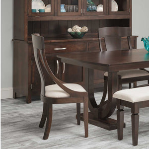 Espresso dining chair with sloped curved arms and a cream cushioned seat, set at a dark trestle table beside a china cabinet