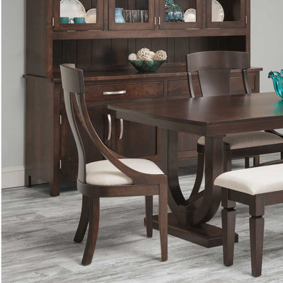 Espresso dining chair with sloped curved arms and a cream cushioned seat, set at a dark trestle table beside a china cabinet