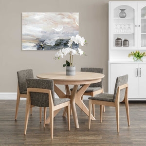 Round mid century modern dining table in a pale finish with a crossed base and four gray upholstered chairs
