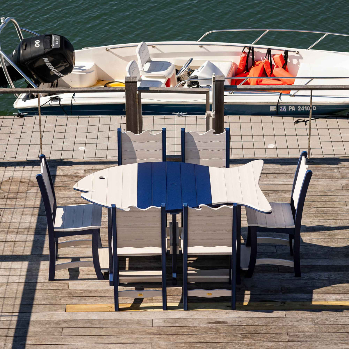 Overhead view of a fish shaped poly counter table in navy and driftwood with six wave back chairs on a dock