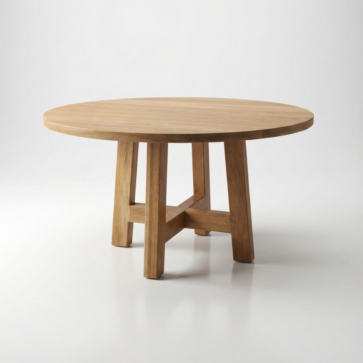 A round wooden dining table with a light natural oak finish, featuring four sturdy legs and a central X-shaped stretcher base, set against a seamless light gray studio background.