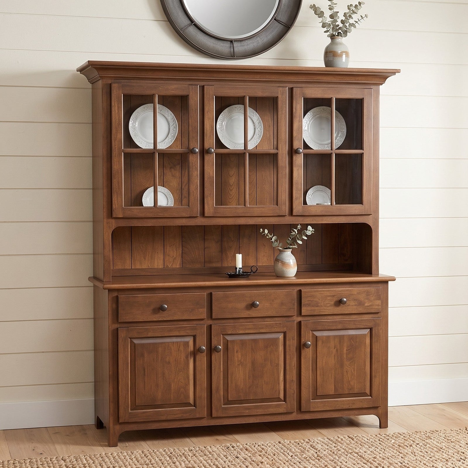 Wooden hutch with glass doors displaying plates against a neutral wall.