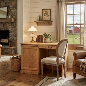 Oak flat top computer desk in a farmhouse room by a window, styled with an oil lamp, books and an ivy plant