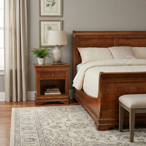 Cherry sleigh bed with a scrolled headboard beside a one-drawer open nightstand and fern in a gray bedroom