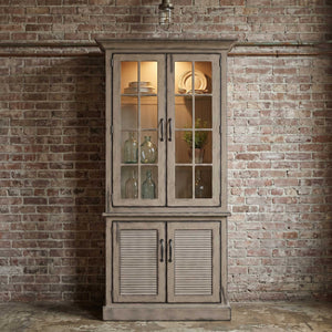 Weathered driftwood gray two-door china cabinet with lit mullioned glass doors, dishes on shelves and louvered base doors