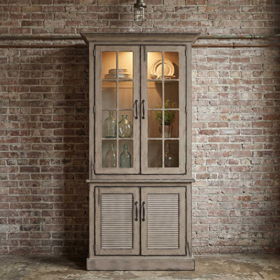 Weathered driftwood gray two-door china cabinet with lit mullioned glass doors, dishes on shelves and louvered base doors