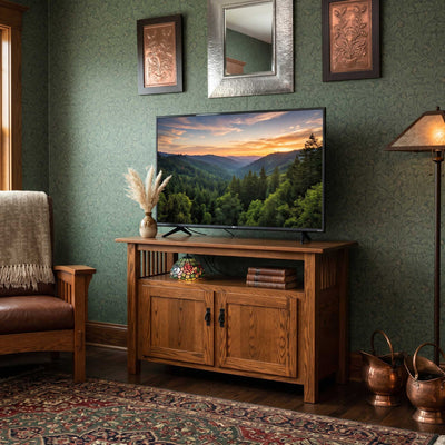 Oak Mission tv console with open shelf and two paneled doors holding a flat screen tv in a green wallpapered room