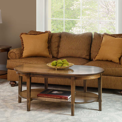 Oval coffee table with a lower display shelf and tapered legs styled in a living room beside a brown chenille sofa