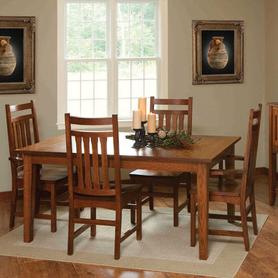 Mission style quartersawn oak leg dining table with slat back chairs, candles and greenery in a sunlit dining room