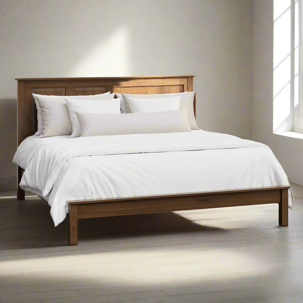 A king-sized solid wood high panel bed frame with a low footboard, shown in a brown stain finish, made with pillows and a bedsheet.