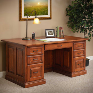Cherry executive desk with lamp and books, framed sunrise painting above and a ficus tree beside it