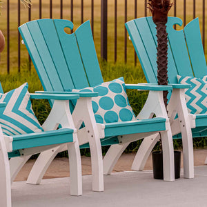 Row of turquoise and white wave back patio chairs with throw pillows beside a pool and palm tree