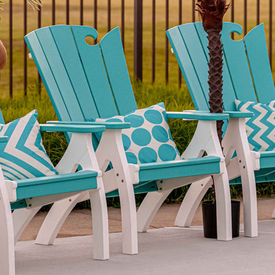 Row of turquoise and white wave back patio chairs with throw pillows beside a pool and palm tree