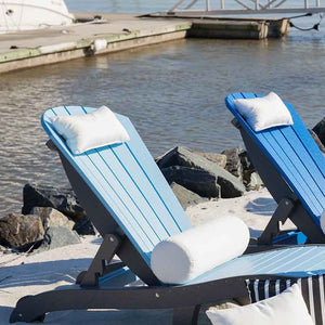 White bolster neck pillows resting on the backs of blue poly chaise lounges at the water's edge