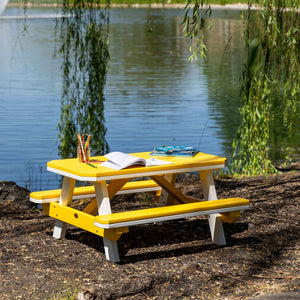 Yellow and white kids poly picnic table with attached benches holding books and pencils beside a pond