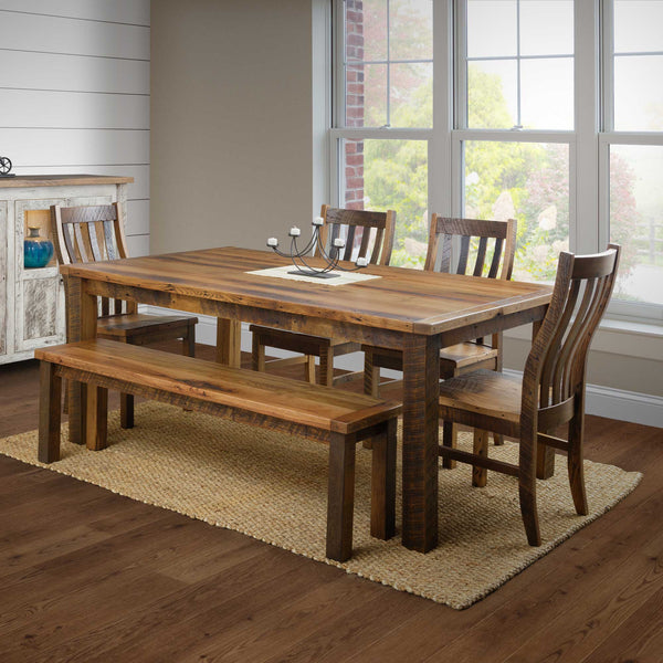A rustic farmhouse dining set made of reclaimed barnwood, including a rectangular dining table, four chairs, and a matching bench, displayed in a room with a window.