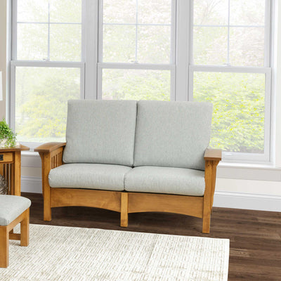Mission oak Morris loveseat with light gray cushions in a bright sunroom with tall windows behind