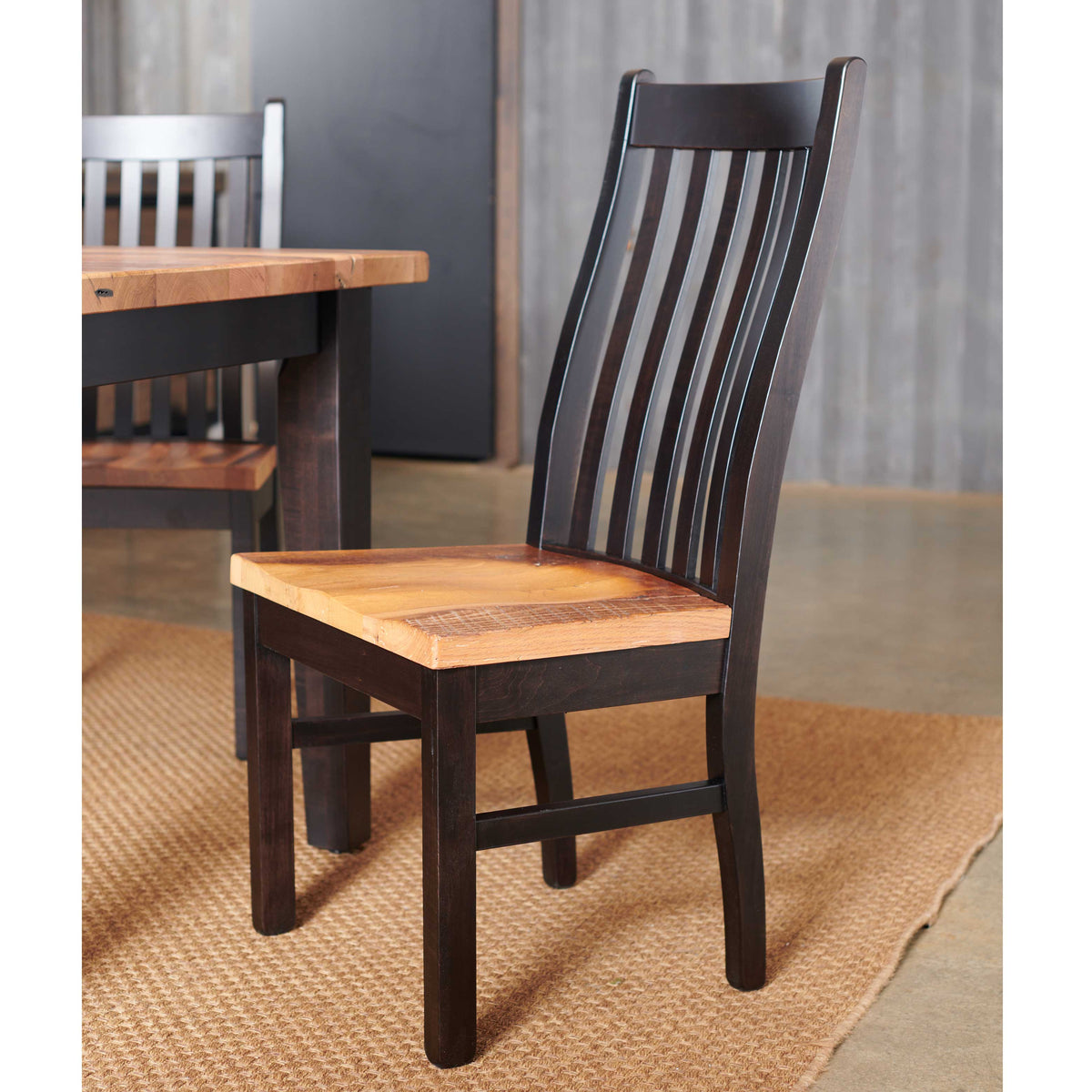 Black slat-back dining chair with natural wood seat beside a reclaimed plank table and bench on a jute rug