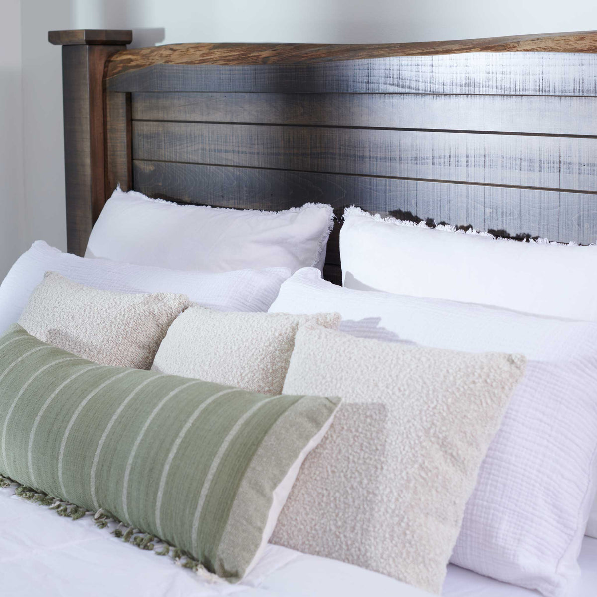 Rough-sawn plank headboard framed in darker wood behind white pillows and green striped and boucle cushions