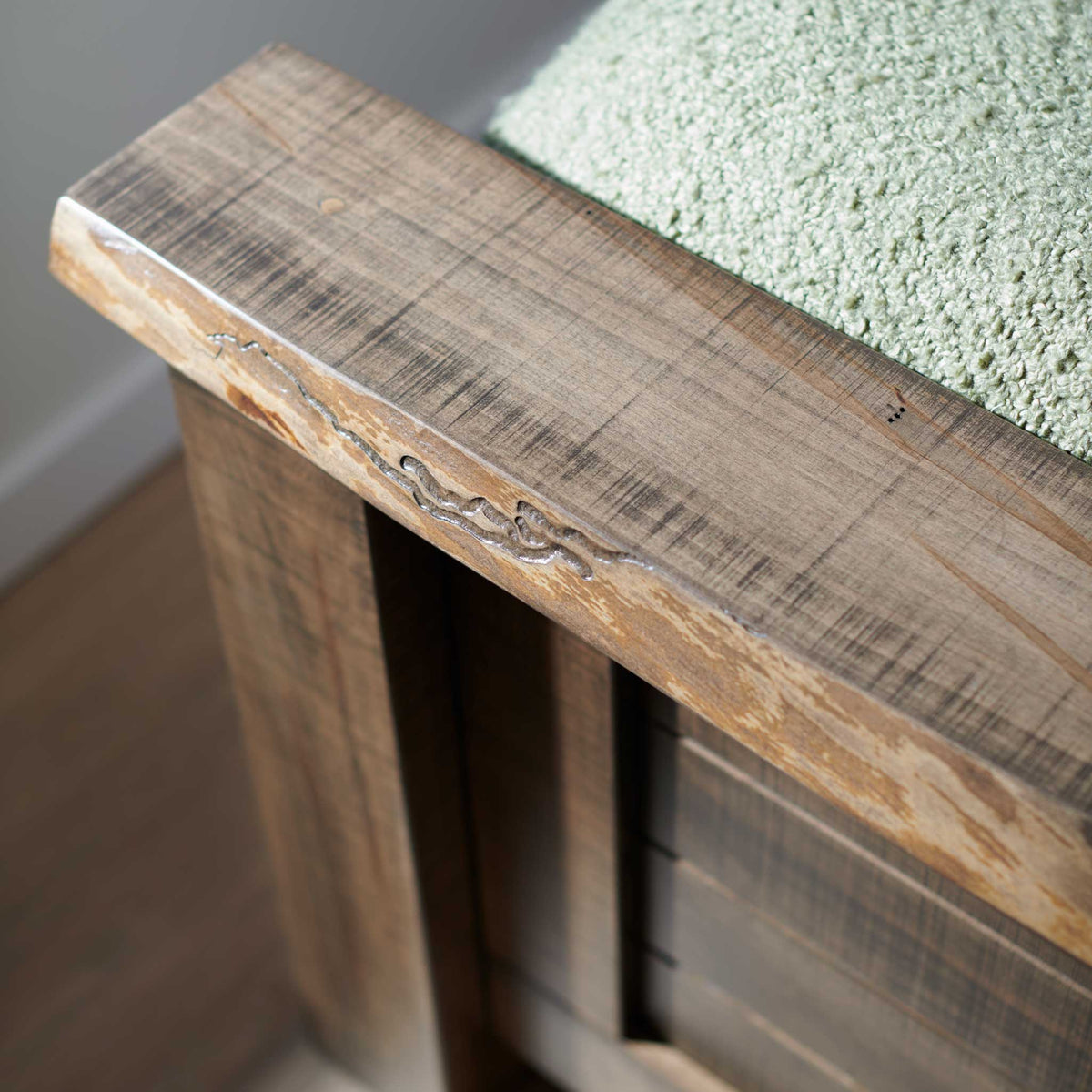 Close-up of the bed's live edge top rail showing rough saw texture, natural fissures and light gray wash finish