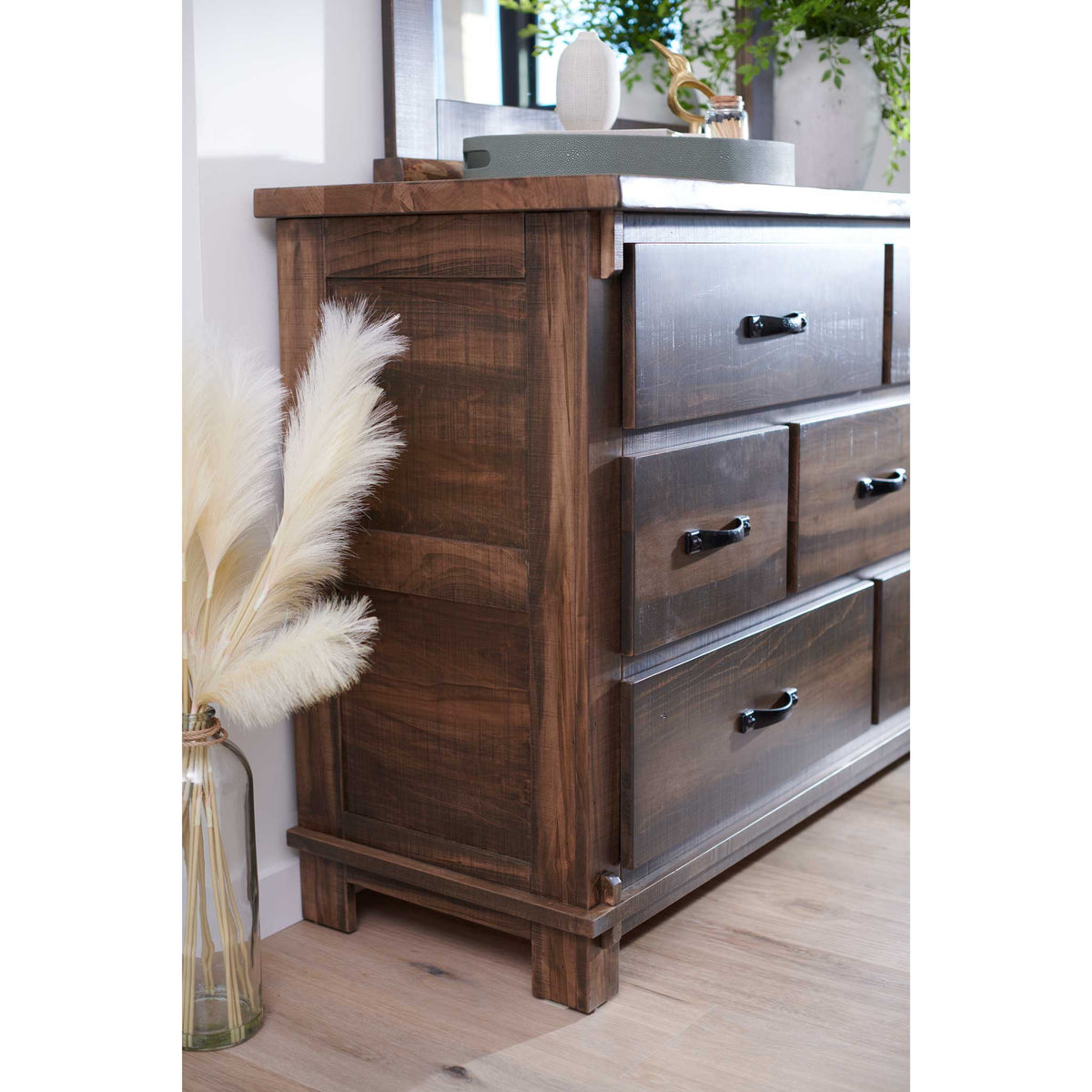 Angled side view of the reclaimed wood dresser showing paneled end panel, plank top and black pulls beside pampas grass