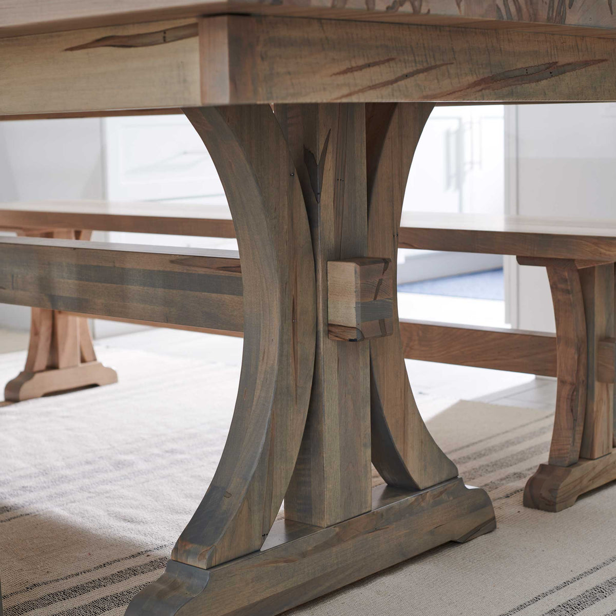 Trestle pedestal detail of the gray-washed dining table with curved legs, tenon key and benches on either side