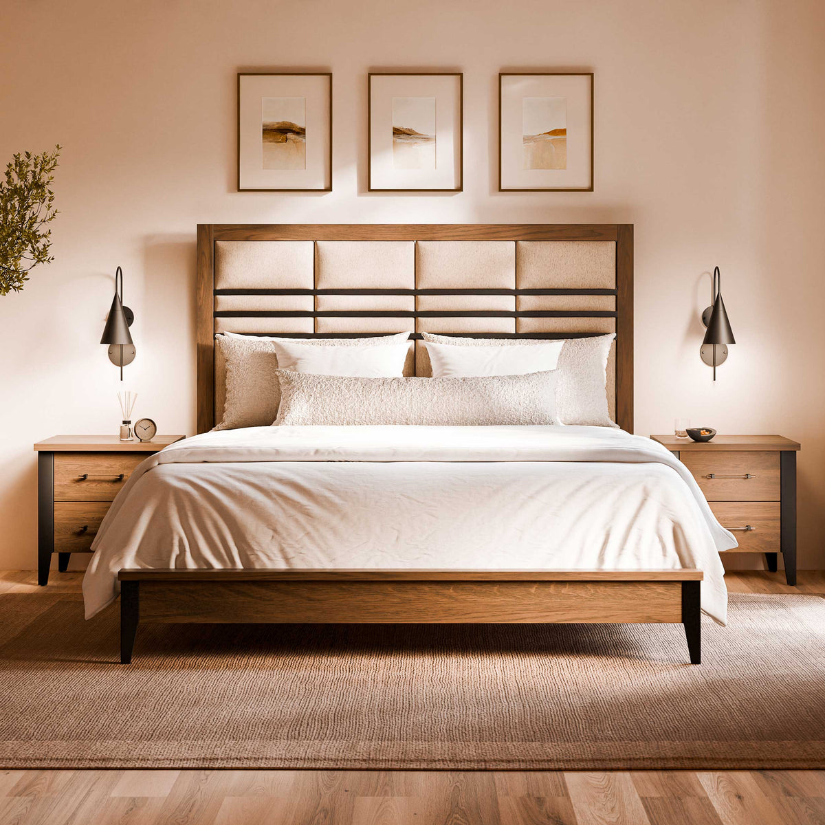 A modern wooden bed frame with a padded headboard, dressed in white bedding, set in a warm neutral bedroom with matching nightstands, wall lamps, and three framed artworks above.