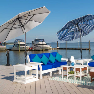 Two market umbrellas over white poly sofas with royal blue cushions, teal pillows and side tables on a marina dock