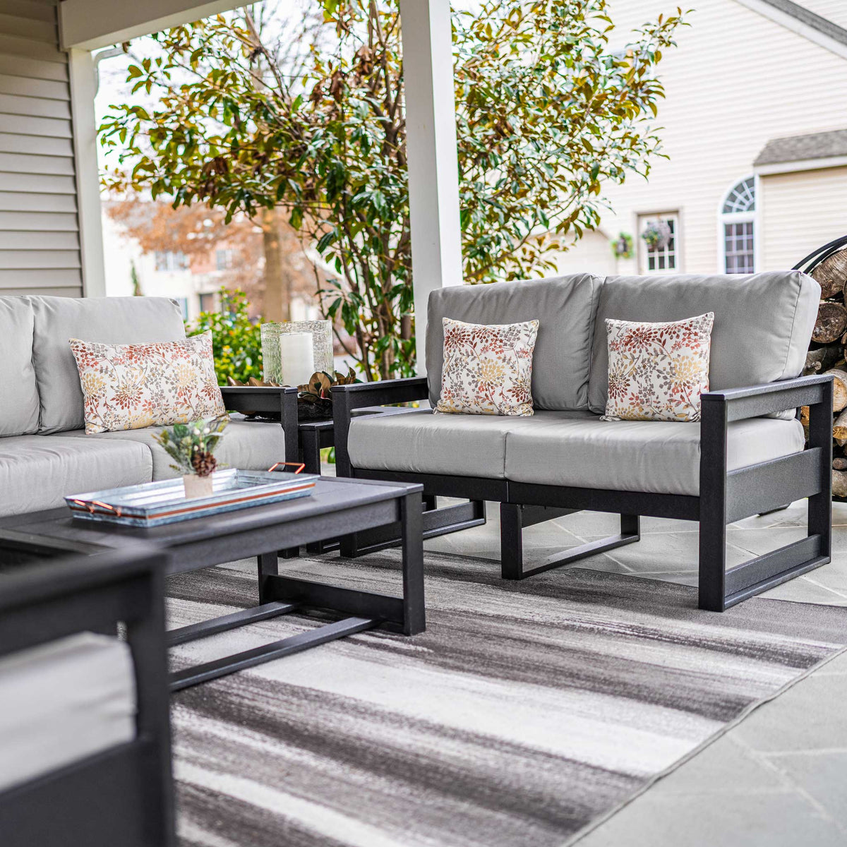 Black poly loveseats with gray cushions and floral pillows facing a coffee table on a covered porch