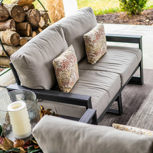 Close view of a black poly sofa with gray cushions, floral pillows and a candle lantern on a porch