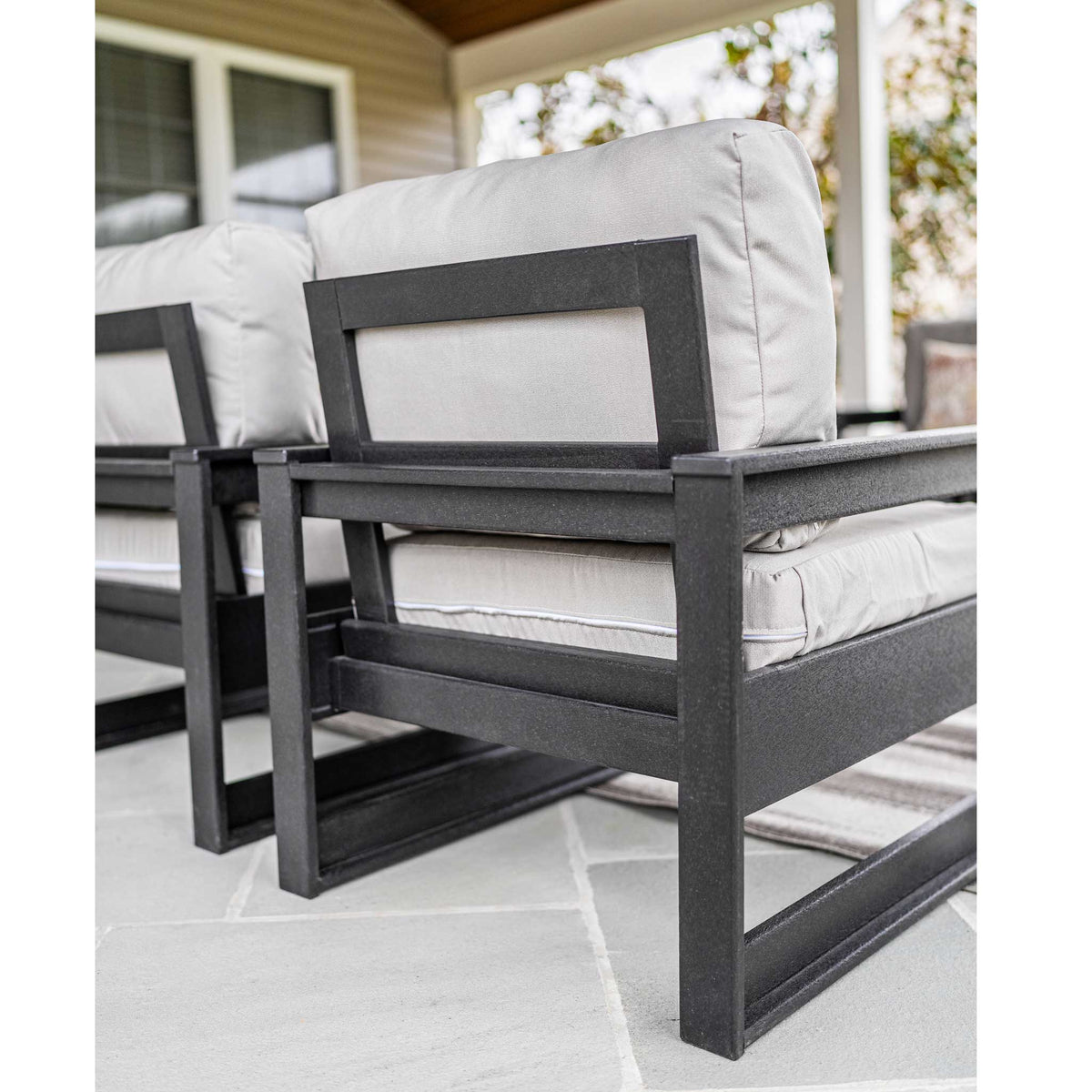 Side view of black poly club chairs with open square frames and thick gray cushions on a porch