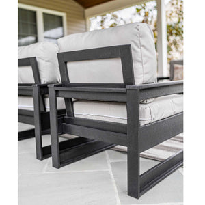 Side view of black poly club chairs with open square frames and thick gray cushions on a porch