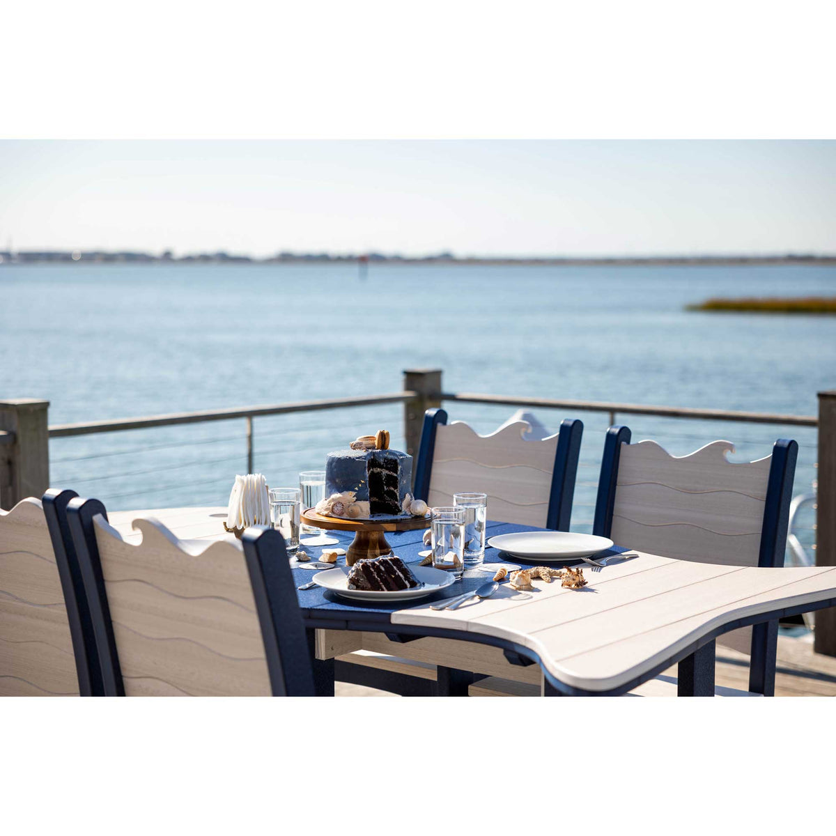 Close view of the wave carved chair backs and driftwood poly tabletop set with cake and glassware by the bay