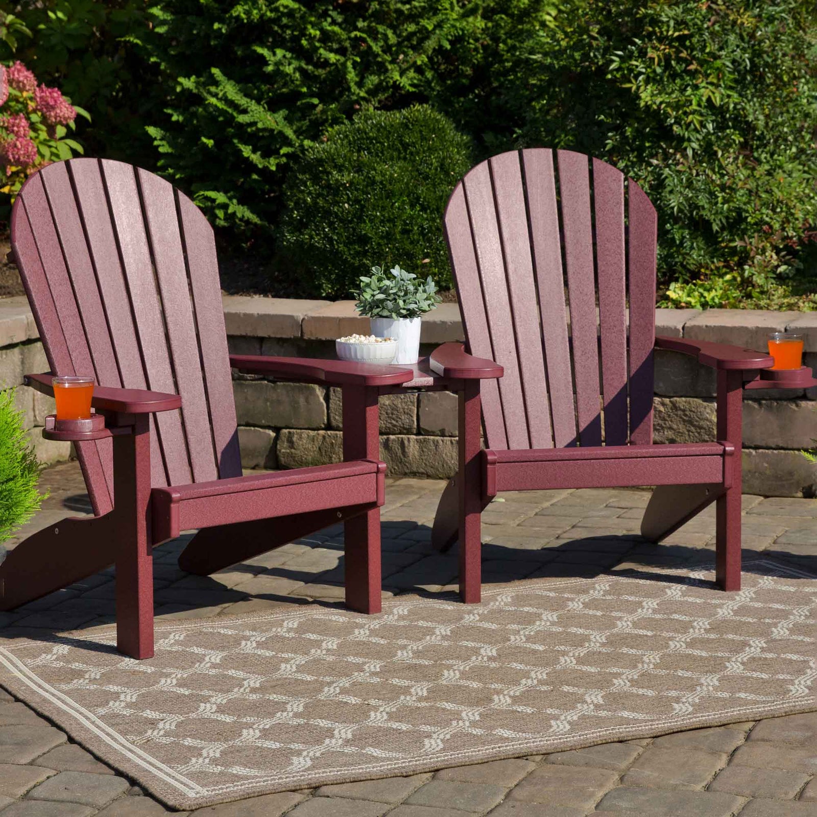 Two cedar and black poly Adirondack chairs with fanned slat backs, cup holders and a shared side table on a patio