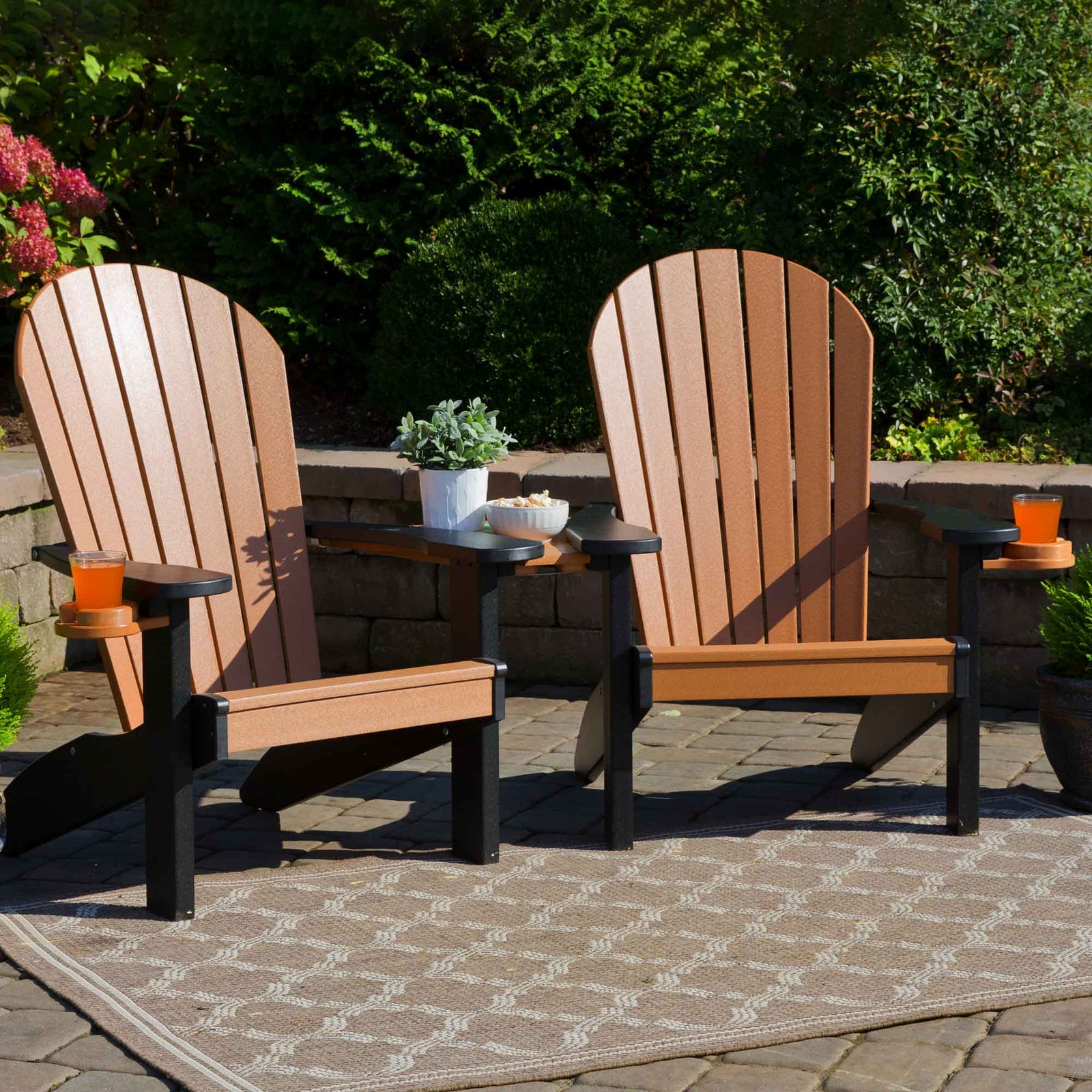 Two cedar and black poly Adirondack chairs with fanned slat backs, cup holders and a shared side table on a patio