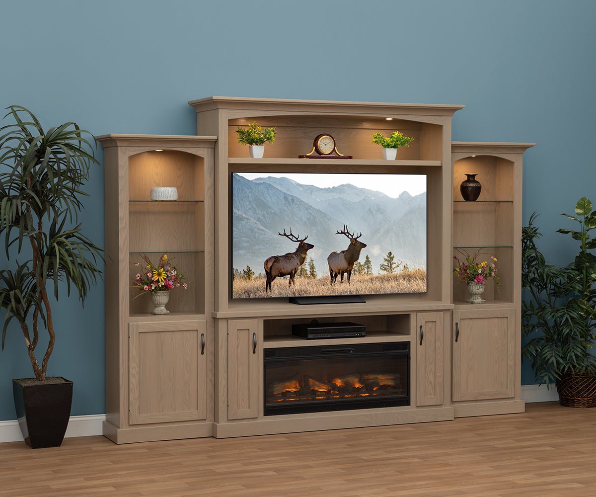 Light stained entertainment center with lighted side towers, electric fireplace beneath the TV and crown topped bridge in a blue room