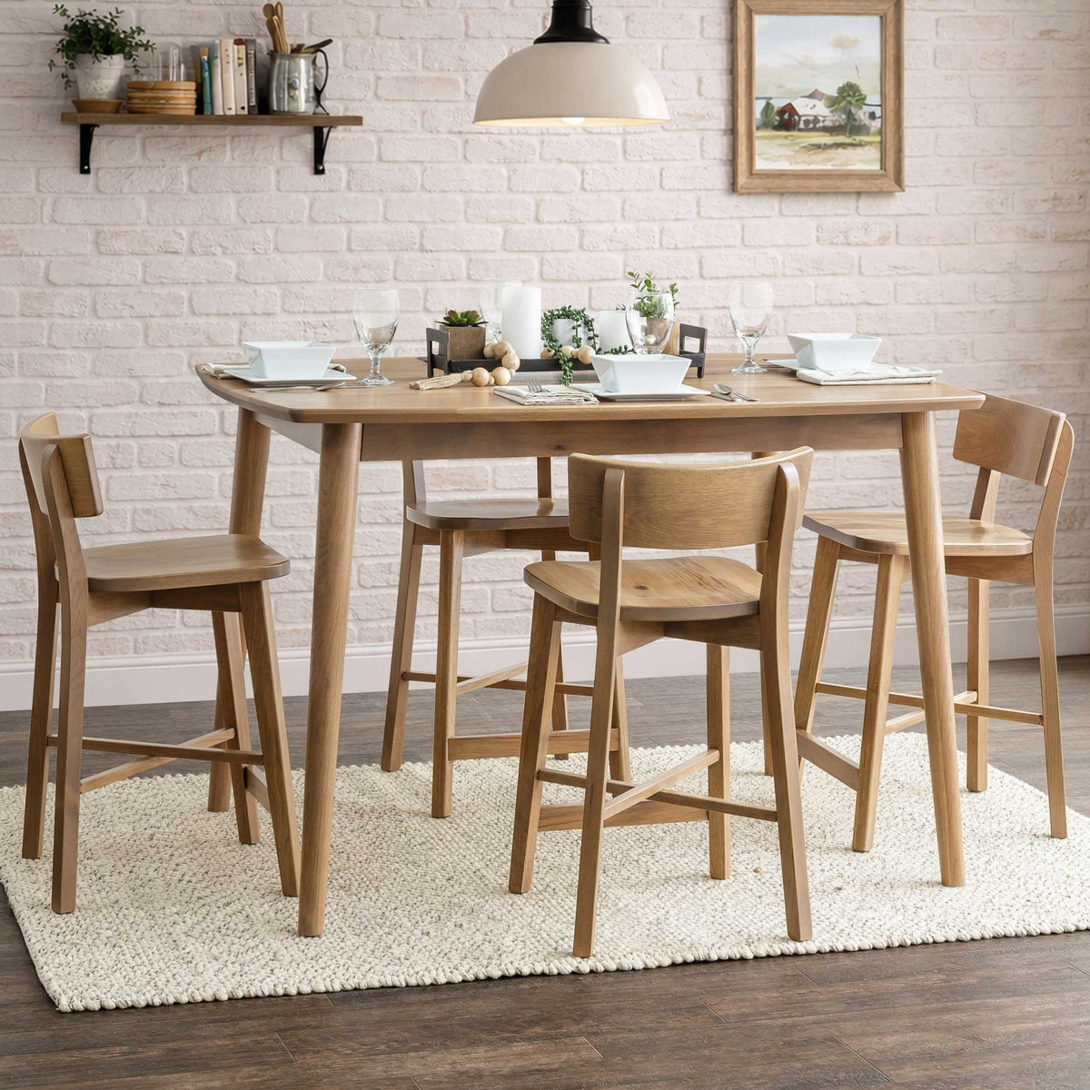 Counter height mid century dining table in light oak with four wood back stools on a woven rug by a brick wall