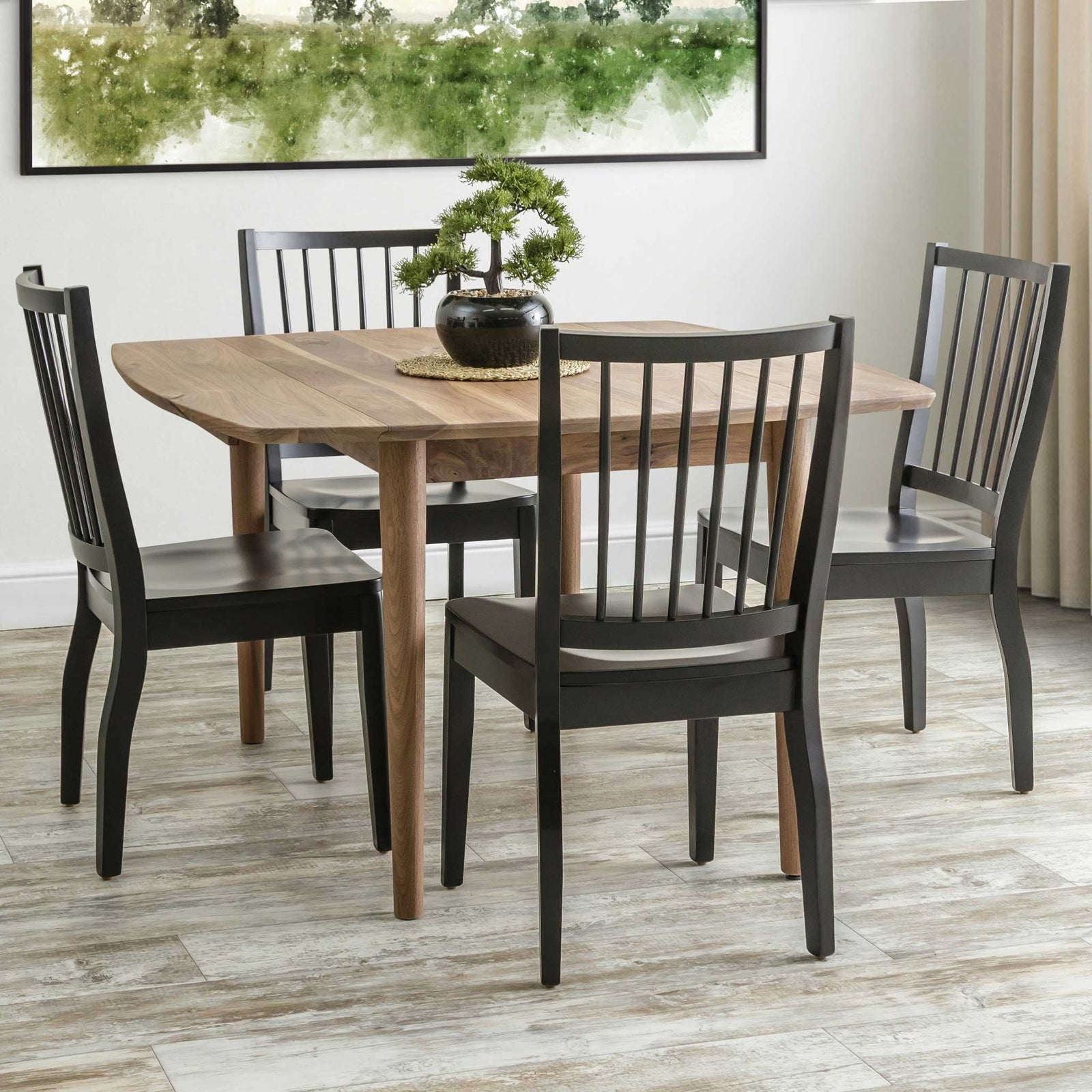Walnut drop leaf dining table with four black slat back chairs in a room with a green landscape painting