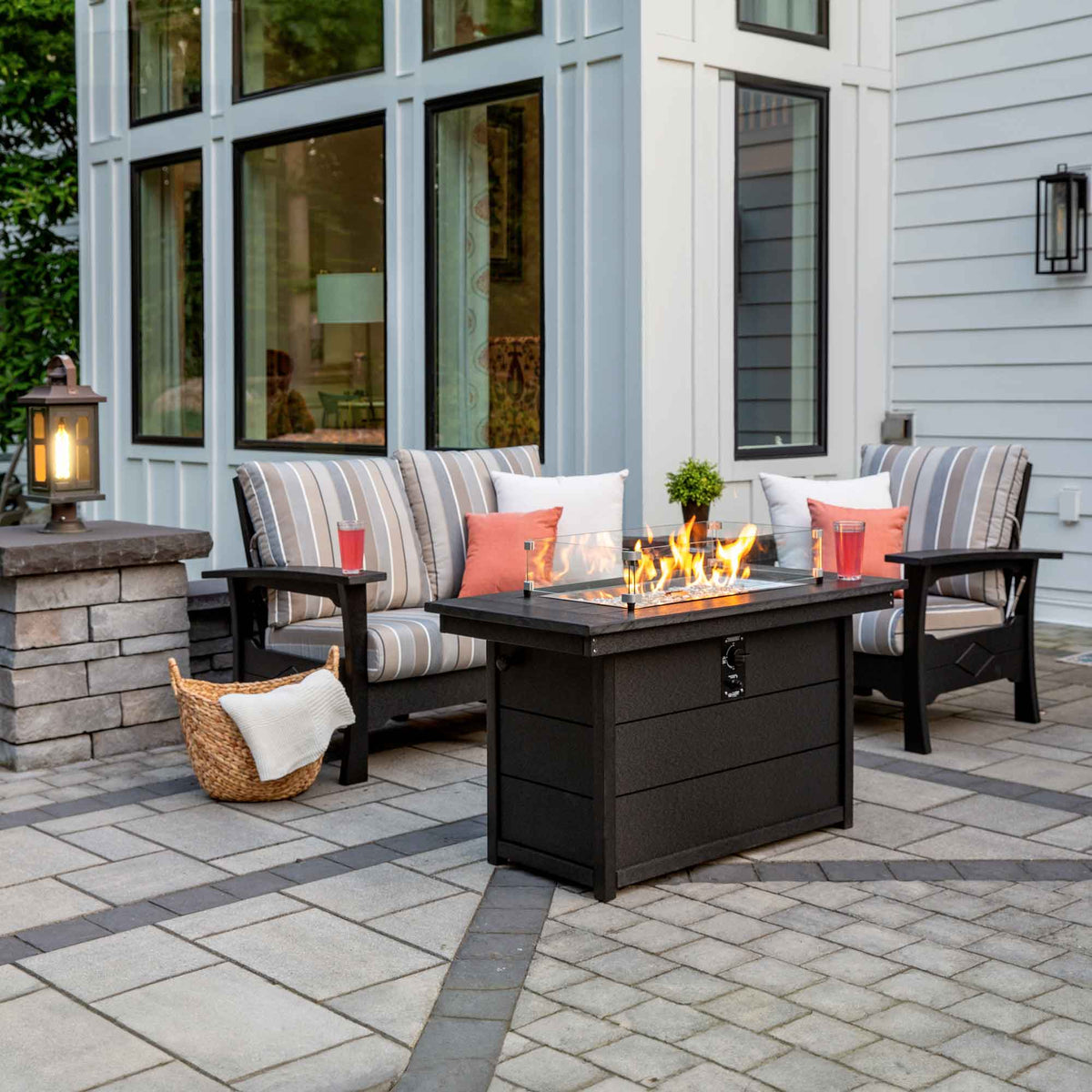 Striped cushion poly patio loveseat and chair flanking a lit rectangular fire pit table on a paver patio